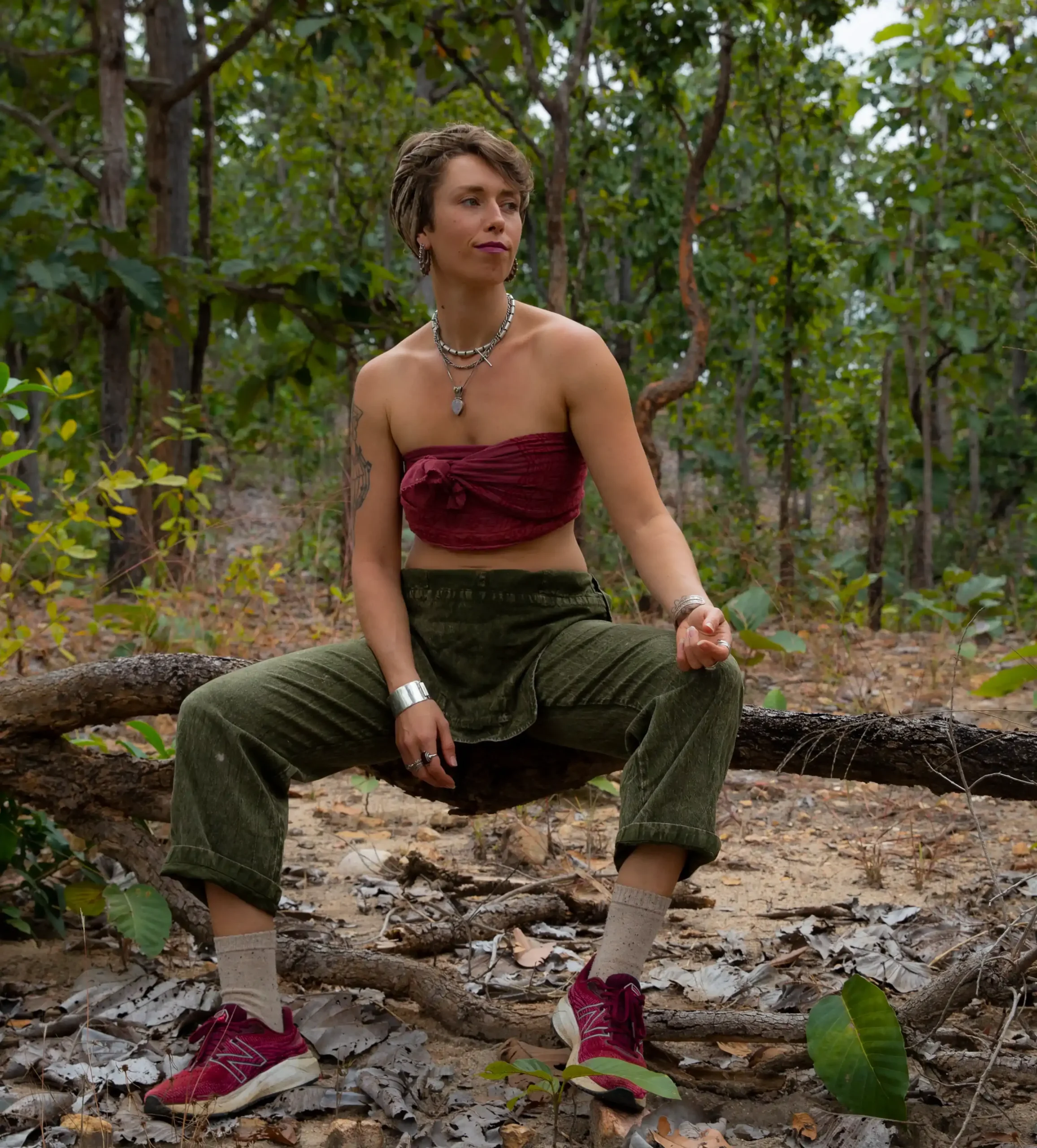 Acoustic and soulful artist Daisy Green in Khaki dungarees and a burgandy crop top sitting in the middle fo a forest in Thailand